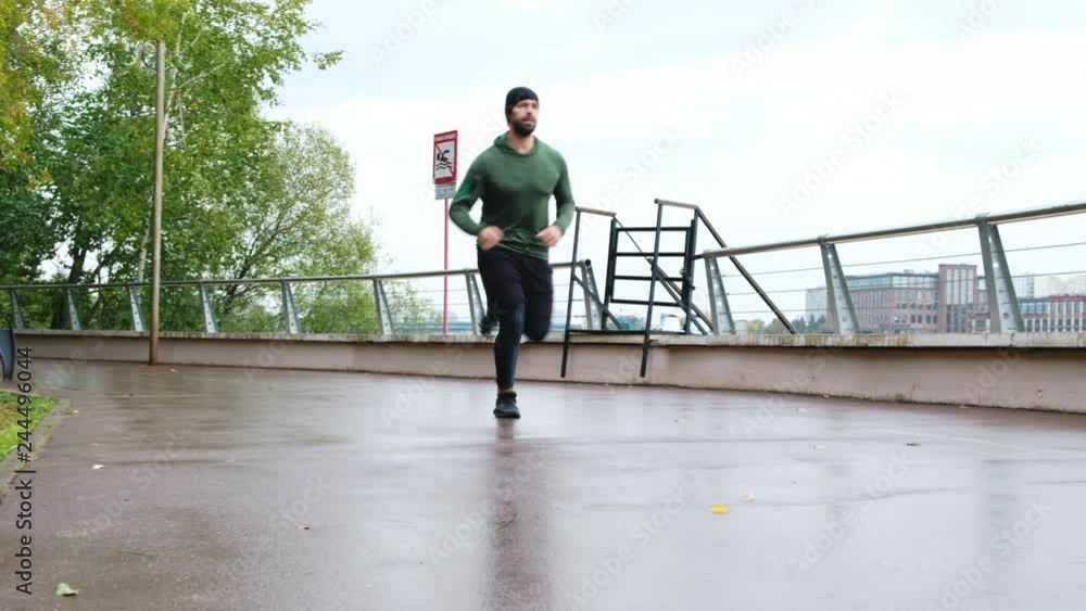 Runner man running on park path exercising on raining day. Fit male fitness model training doing recreational jogging workout Runner man running on park path exercising on raining day. Fit male fitness model training doing recreational jogging workout