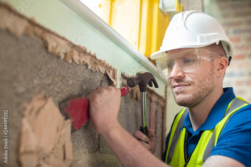 Obraz na plátne Construction Worker With Chisel Removing Plaster From Wall In Renovated House