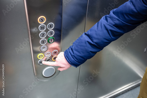 man in a blue jacket in the elevator presses his finger on the button to close the door