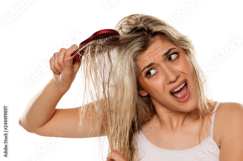 desperate blond woman combing her messy wet hair on white background