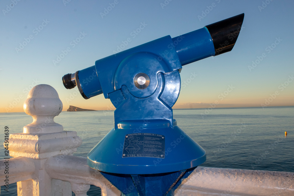 The famous blue telescope situated at the look out point Balcón del Mediterráneo & Mirador del Castell in Benidorm Alicante in Spain with Mirador de la Isla de Benidorm in the background.