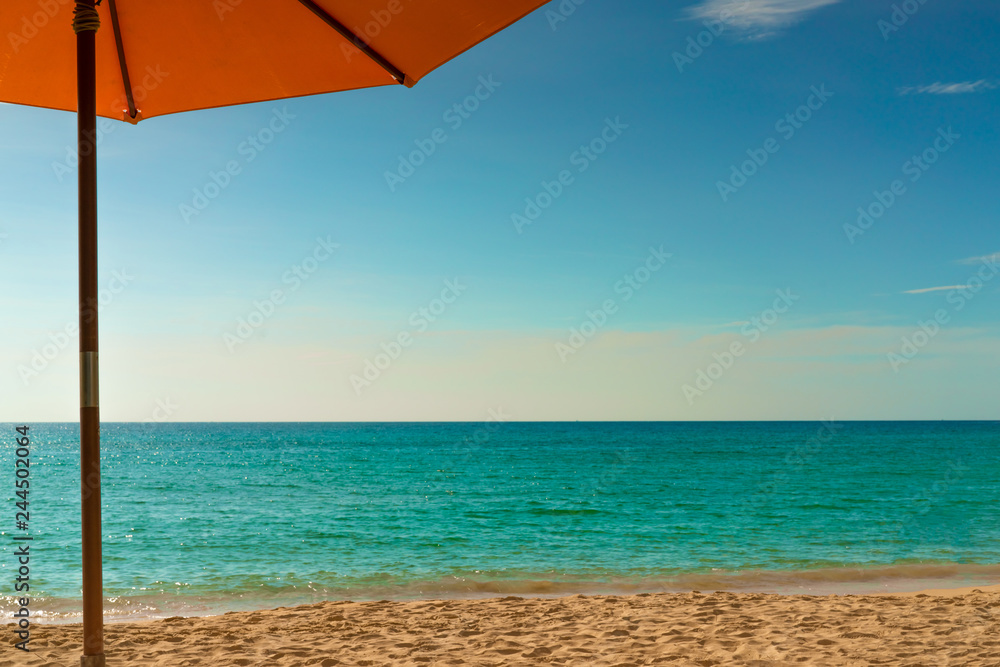 Orange beach umbrella on golden sand beach by the sea with emerald green sea water and blue sky and white clouds. Summer vacation on tropical paradise beach concept. Skyline between sea and sky.