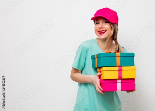 Beautiful young girl in pink cap and blue t-shirt with holiday present boxes on white background.