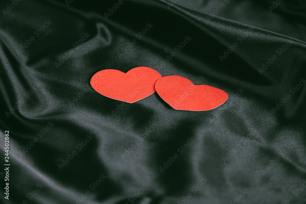 Fototapeta premium two red hearts on a black silk background.