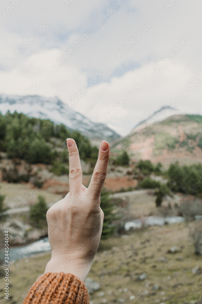 Woman showing two gesture near valley with high hills in cloudy weather Woman showing two gesture near valley with high hills in cloudy weather