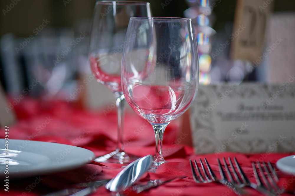 Fine dining table setting with white china and wine and water crystal glasses, with silverware in the order of use, and romantic red tablecloth ready for guests at an event, wedding or at a restaurant