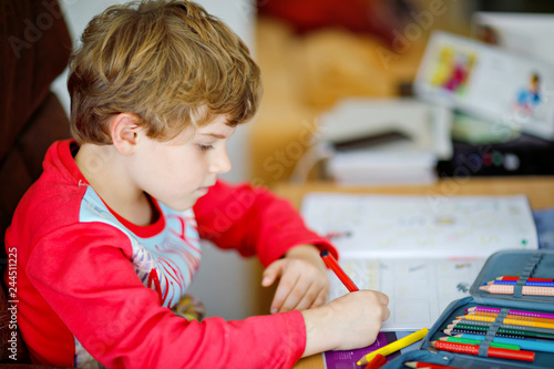 Portrait of cute happy school kid boy at home making homework. Little child writing with colorful pencils, indoors. Elementary school and education. Kid learning writing letters and numbers