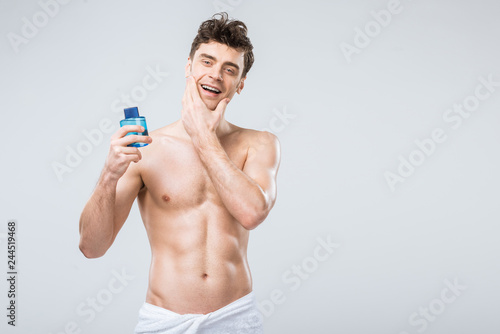 happy shirtless man holding bottle with cologne, isolated on grey