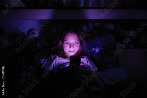 Little girl at night under a blanket looking at the smartphone.