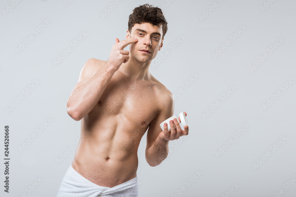 handsome shirtless man applying cosmetic cream on face, isolated on grey handsome shirtless man applying cosmetic cream on face, isolated on grey