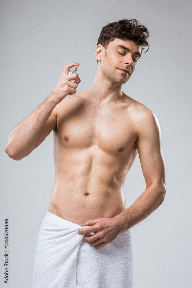 shirtless sexy man spraying perfumes, isolated on grey