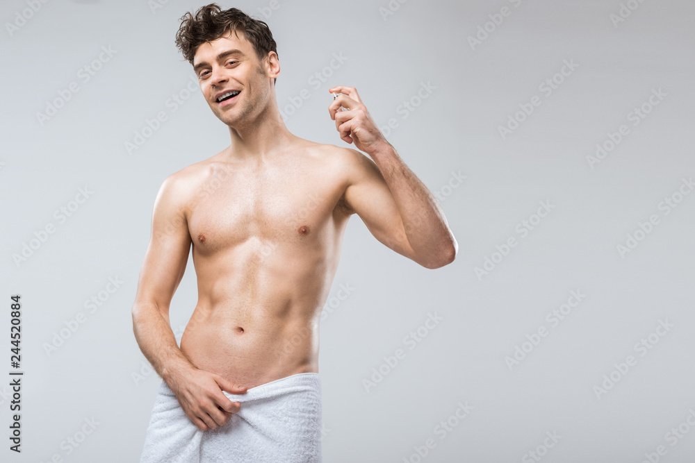 Fototapeta premium wesoły przystojny mężczyzna rozpylania perfum, na szarym tle