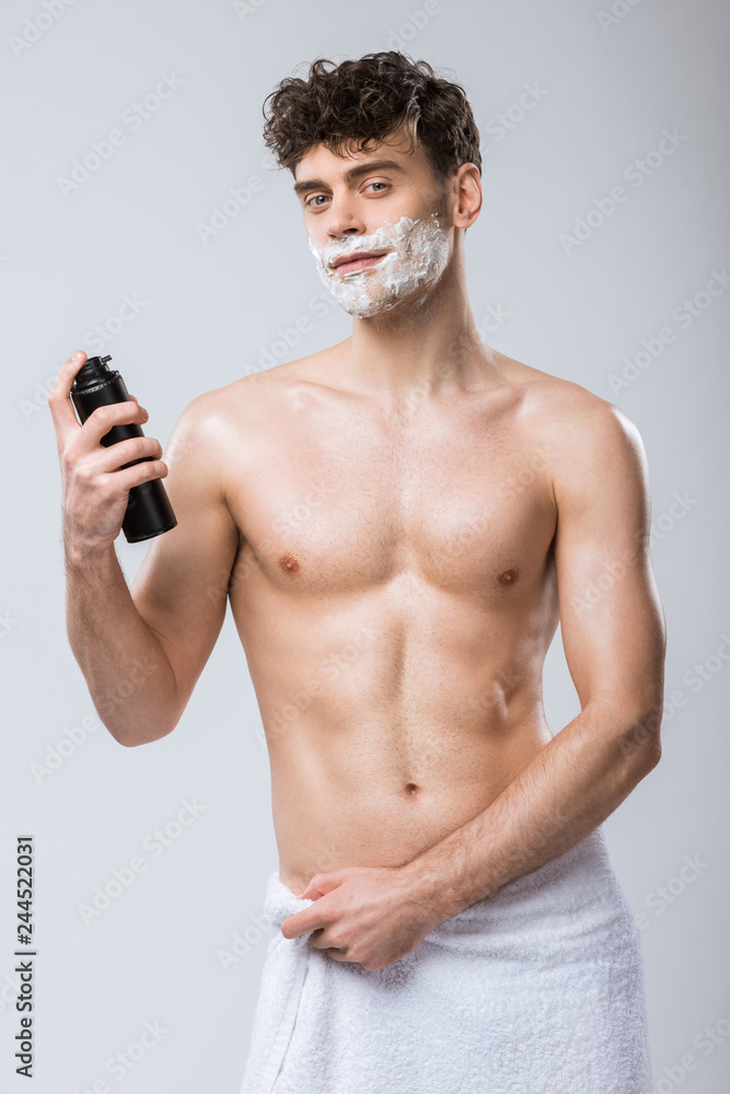 Fototapeta premium handsome shirtless young man holding bottle with shaving foam, isolated on grey