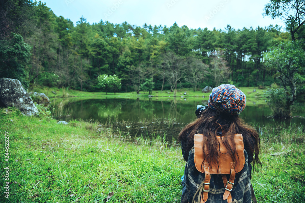 Fototapeta premium Young women travel nature. she sat on the waterfront lawn at the public park Photographing beautiful landscape..