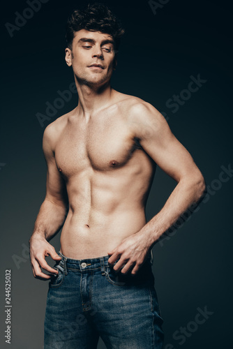 sexy handsome man in jeans posing isolated on dark grey