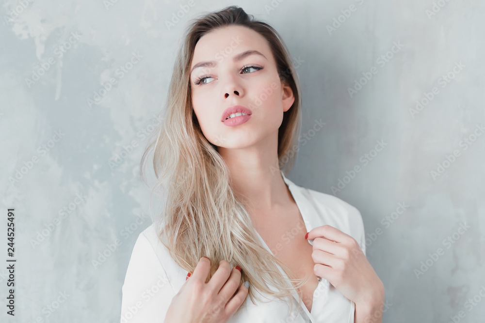Model blonde blue jeans white shirt standing gray wall by window openness comfort portrait positive copy space.