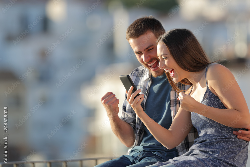 Fototapeta premium Excited couple celebrating online phone news outdoors