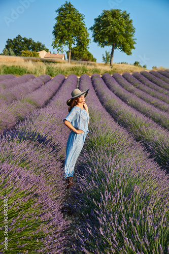 The beautiful young girl in a blue dress walks across the field of a lavender, long curly hair, smile, pleasure, mountains on background, a house of the gardener, trees, perspective of a lavender