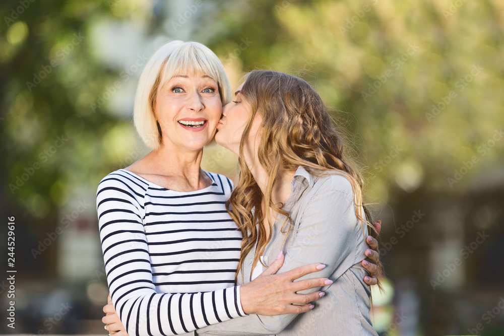 Fototapeta premium Woman kissing elderly mother outdoors on sunny day