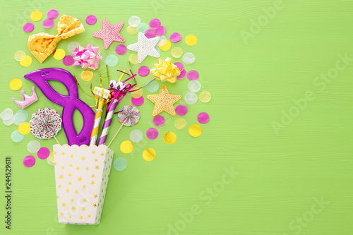 carnival party celebration concept with mask and colorful party accessories over green wooden background. Top view. Flat lay.
