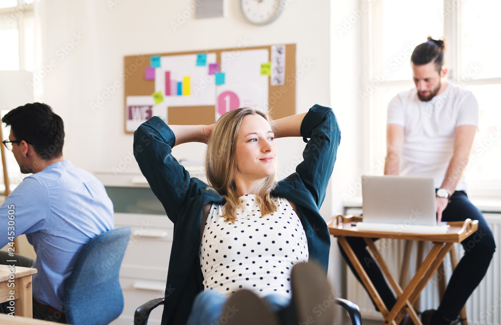 Obraz premium Portrait of young relaxed businesswoman with colleagues in a office, feet on desk.