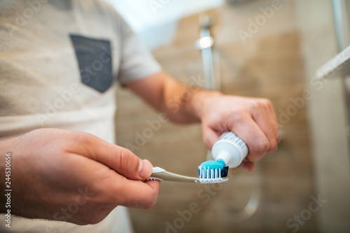 Young man holding a toothbrush and placing toothpaste on it, close-up.