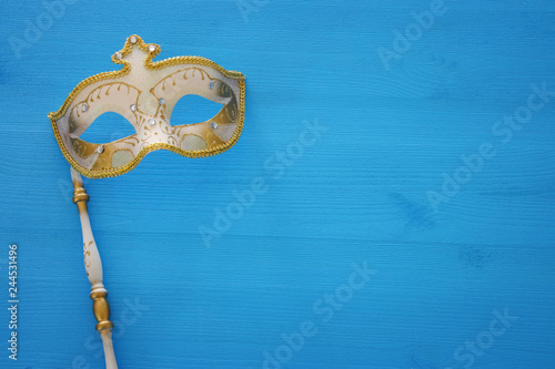 carnival party celebration concept with elegant gold mask on stick over blue wooden background. Top view
