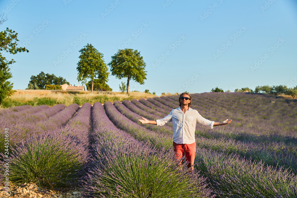 The beautiful brutal young man with long brunette hair poses in the field of lavender.