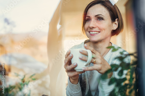 A young woman with cup of coffee looking out of a window. Shot through glass.