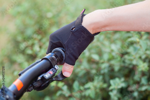 A girl in bicycle gloves holds her hand on the handlebars, clamping the brakes.