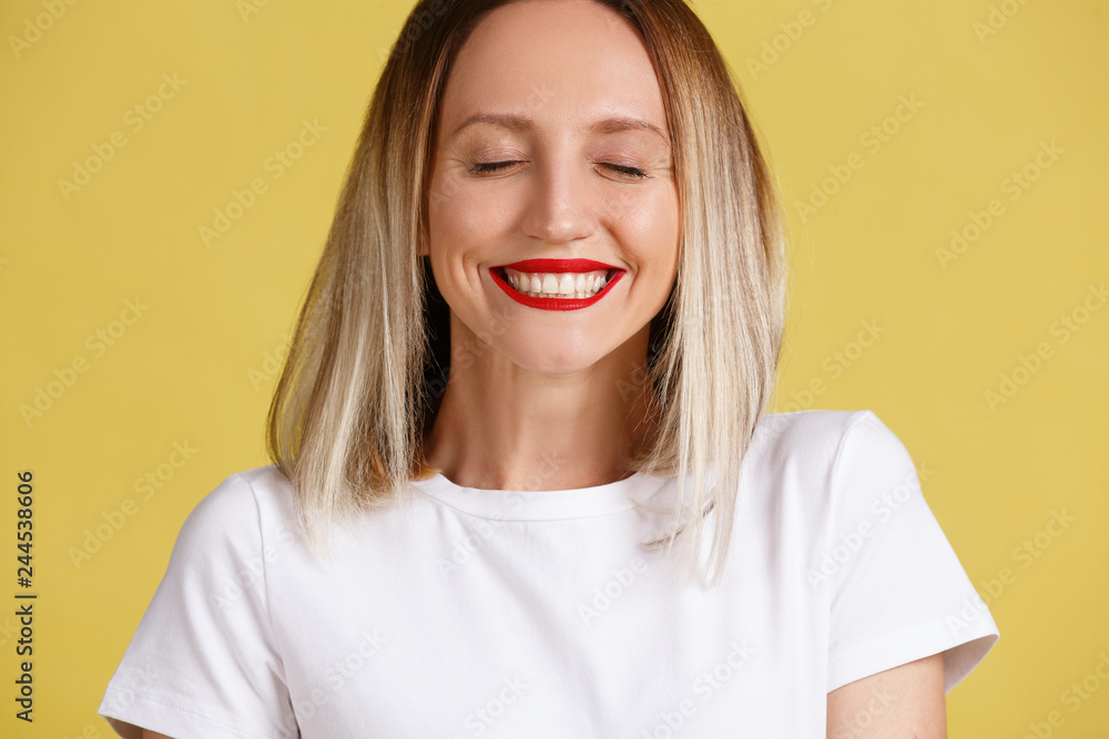 Close-up portrait of a positive smiling young blond woman with close eyes on a yellow background. Place for advertising Close-up portrait of a positive smiling young blond woman with close eyes on a yellow background. Place for advertising