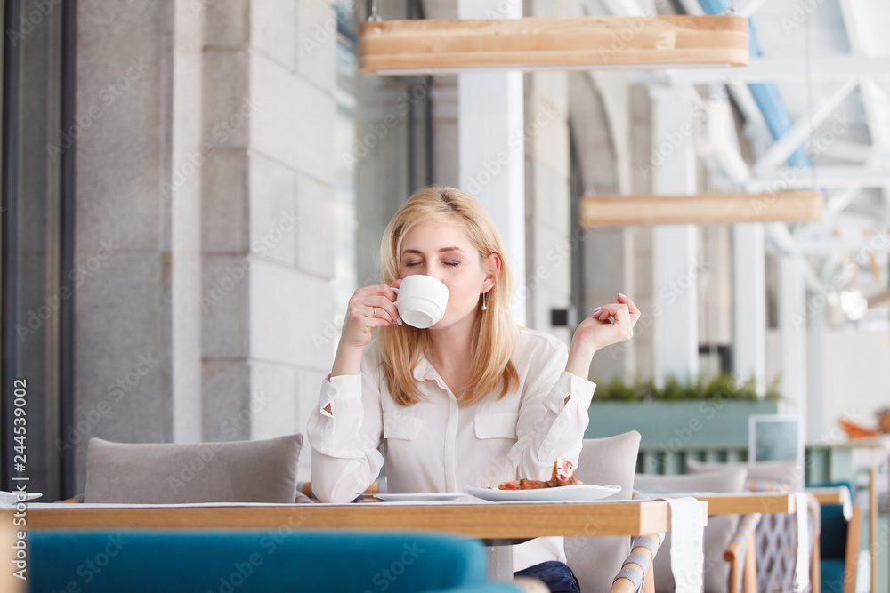 Obraz premium Beautiful successful young businesswoman sits at the table of a street cafe and drinks coffee in good mood in the morning.