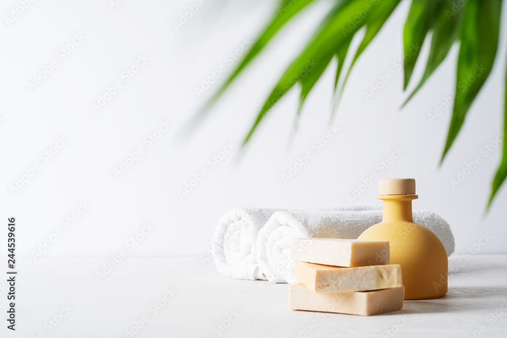 Spa concept: beautiful ceramic bottle, handmade organic soap, white towels and palm leaf on concrete light surface with copy space.