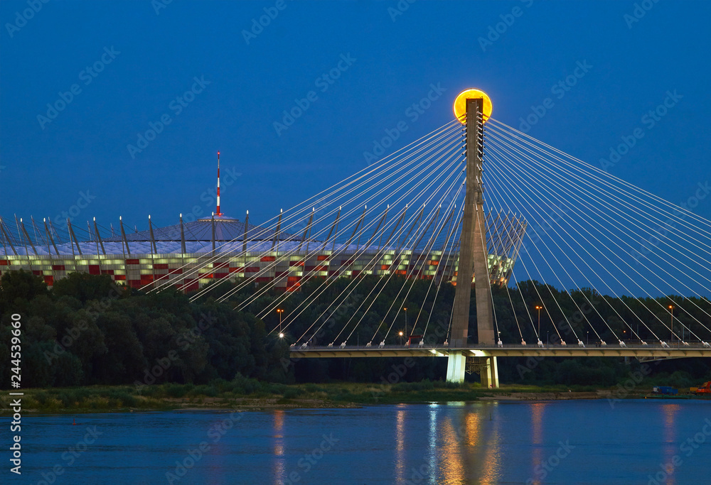 Obraz premium Warszawa, Polska - 20 lipca 2016: Panoramiczny widok wschodzącego słońca nad Stadionem Narodowym i Mostem Świętokrzyskim w stolicy Polski.