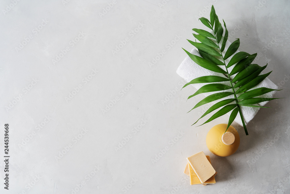 Spa concept: beautiful ceramic bottle, handmade organic soap, white towels and palm leaf on concrete light surface with copy space, flat lay. - obrazy, fototapety, plakaty 