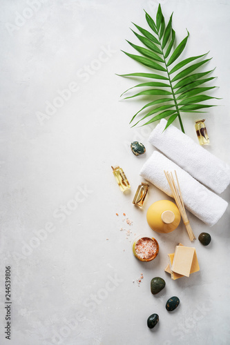 Flat lay spa composition with palm tropical leaf, towels, aroma fragrance bottle, handmade organic soaps, oil frangipani, sandal wood, patchouli, pink salt on light concrete surface with copy space.