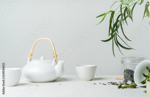 Asian tea concept, two white cups of tea and teapot surrounded with green tea dry leaves , space for a text on white background. Brewing and Drinking tea.