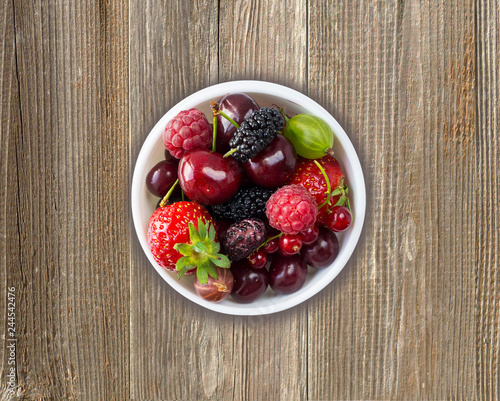 Fruits and berries in bowl on wooden background. Mix berries on rustic background. 