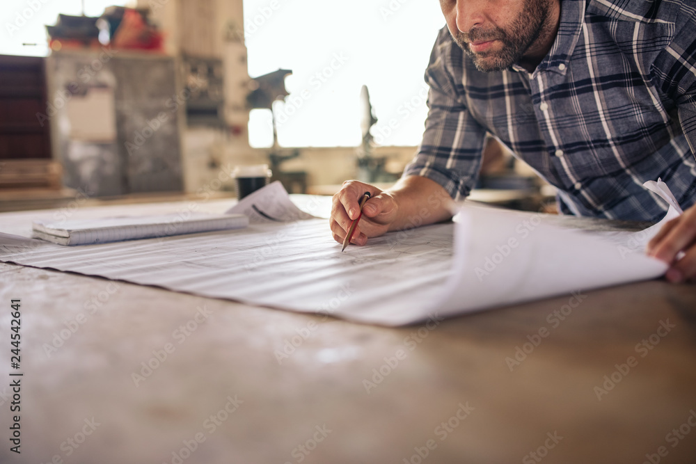 Woodworker leaning over a bench reading furniture design blueprints Woodworker leaning over a bench reading furniture design blueprints