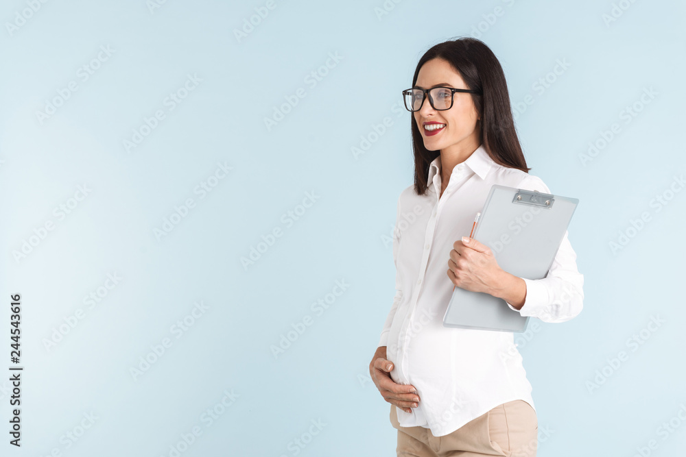 Pregnant business woman isolated over blue wall background holding clipboard. Pregnant business woman isolated over blue wall background holding clipboard.