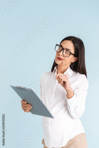 Young pregnant business woman isolated over blue wall background holding clipboard.