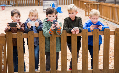 Kids playing with smartphones near wooden fence