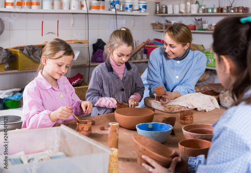 teacher helping teenagers at making pottery during arts and crafts class