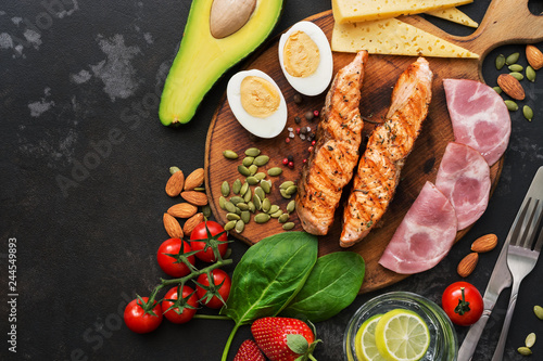 Photos Keto lunch or dinner - grilled salmon, vegetables, boiled egg, water with lime, nuts, ham and cheese on a dark background