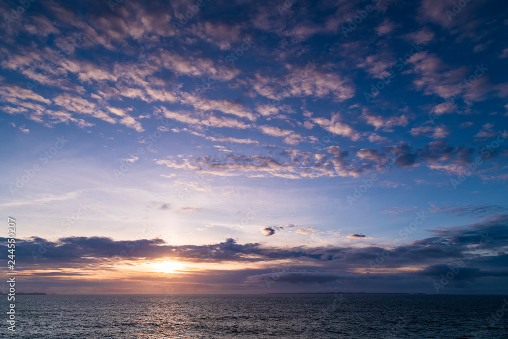 Fototapeta premium The sun setting over the Sea of the Hebides under a Mackerel sky above, from Ardnamurchan, Scotland.