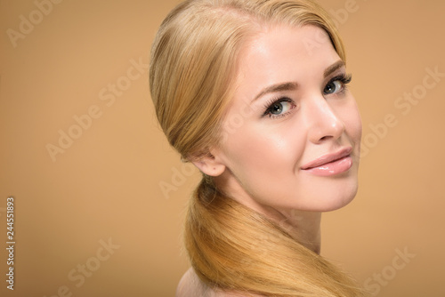 close-up view of attractive blonde girl with long hair smiling at camera isolated on beige