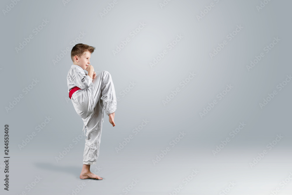 Creative background, a child in a white kimono makes a kick, on a light background. The concept of martial arts, karate, sports since childhood, discipline, first place, victory. copy space.