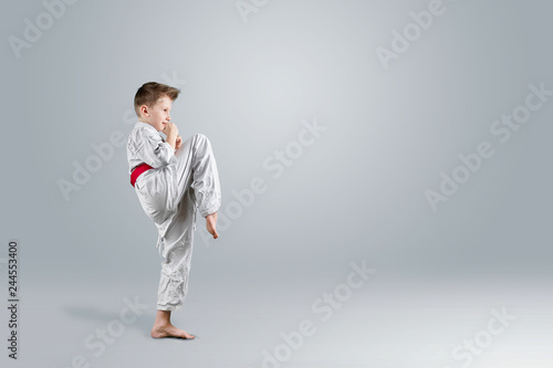 Creative background, a child in a white kimono makes a kick, on a light background. The concept of martial arts, karate, sports since childhood, discipline, first place, victory. copy space.