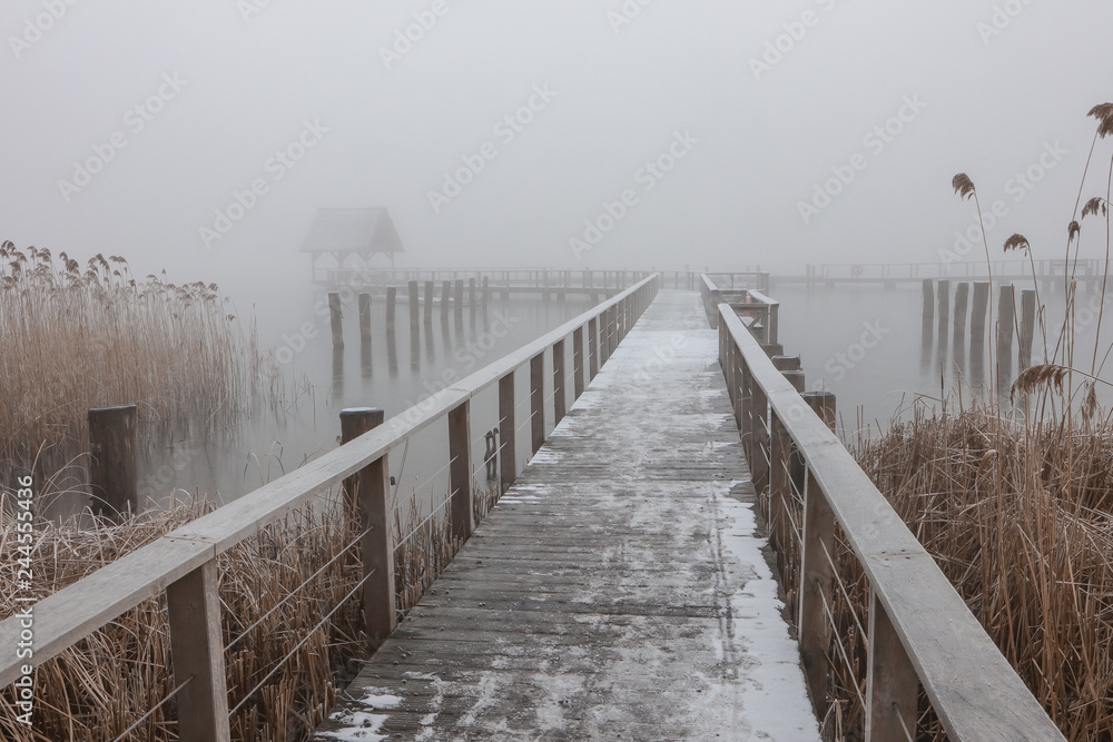 romantischer Steg am See mit Nebel im Winter