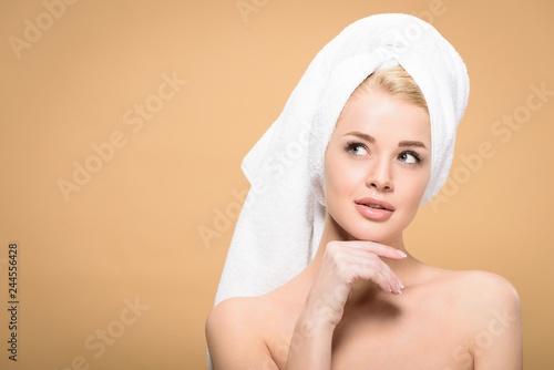 pensive naked girl with towel on head standing with hand on chin and looking away isolated on beige